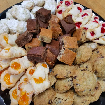 An overflowing platter of moist chocolate chip blondie brownies, soft chocolate chip cookies, flakey Kolacky cookies with jams and powdered sugar snowball cookies.